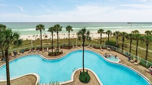 A swimming pool with a beach view, palm trees, and a pier in the background.