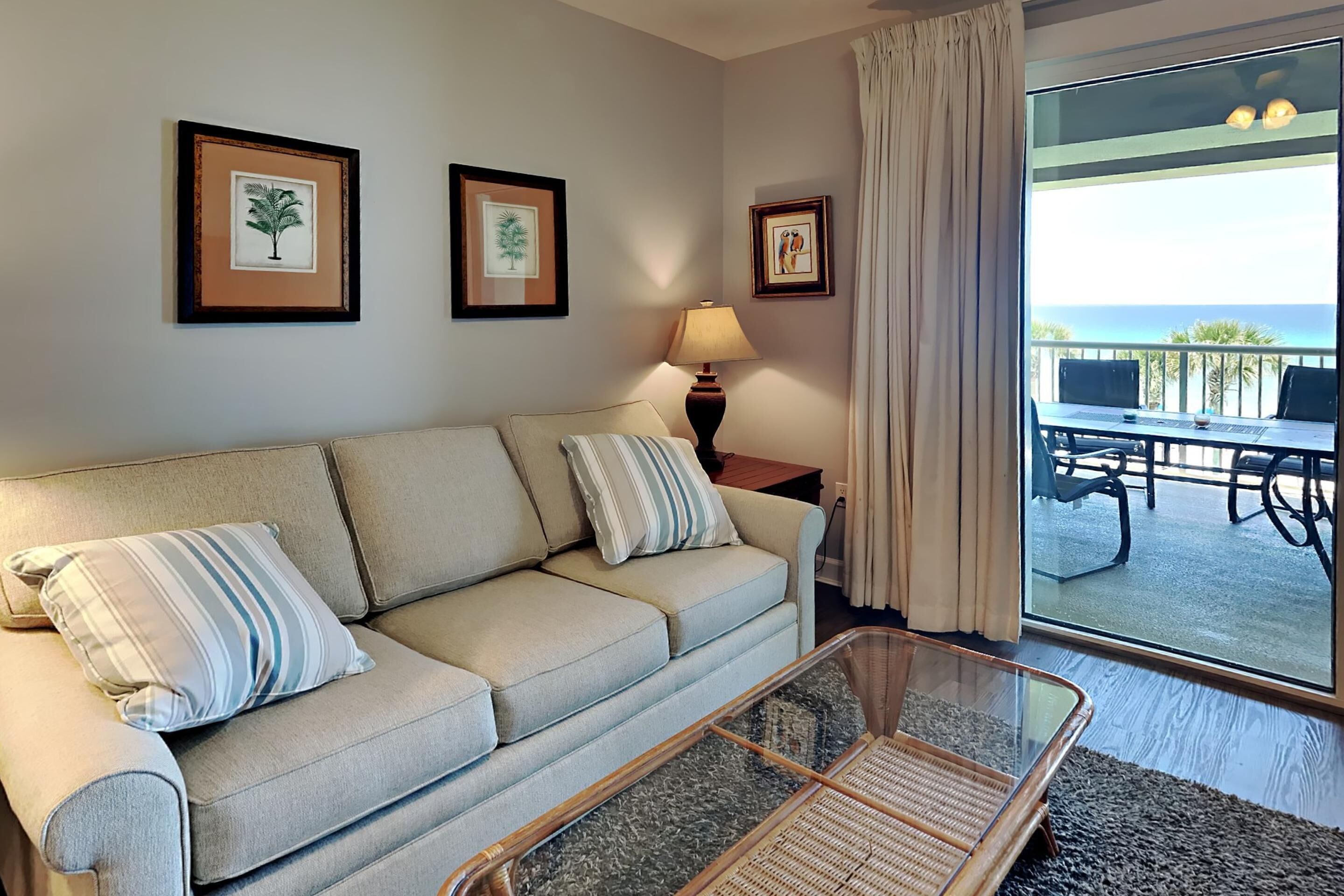 A living room with a beige sofa, striped pillows, a glass coffee table, and framed artwork on the wall.