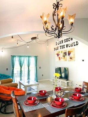 Uma área de refeições com um candelabro, uma parede com uma frase motivacional e uma mesa de jantar posta com tigelas vermelhas.