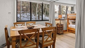Una habitación acogedora con una mesa de comedor, sillas, una cama litera y un ventanal con vistas nevadas.