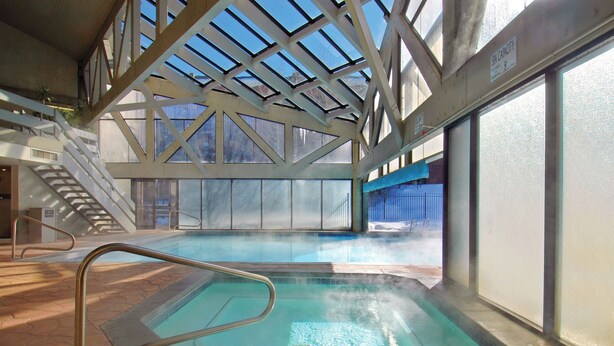 Una piscina interior con techos altos y tragaluces, rodeada de paredes y una escalera.