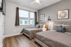 A bedroom with two beds, a ceiling fan, and a large window with curtains.