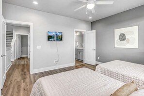 Une chambre avec deux lits, un ventilateur de plafond, une télévision et une salle de bain visible à travers une porte ouverte.