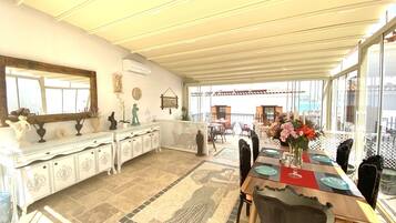 Un patio cubierto con una mesa de comedor lista para cuatro, un mueble blanco decorativo y un suelo de mosaicos.