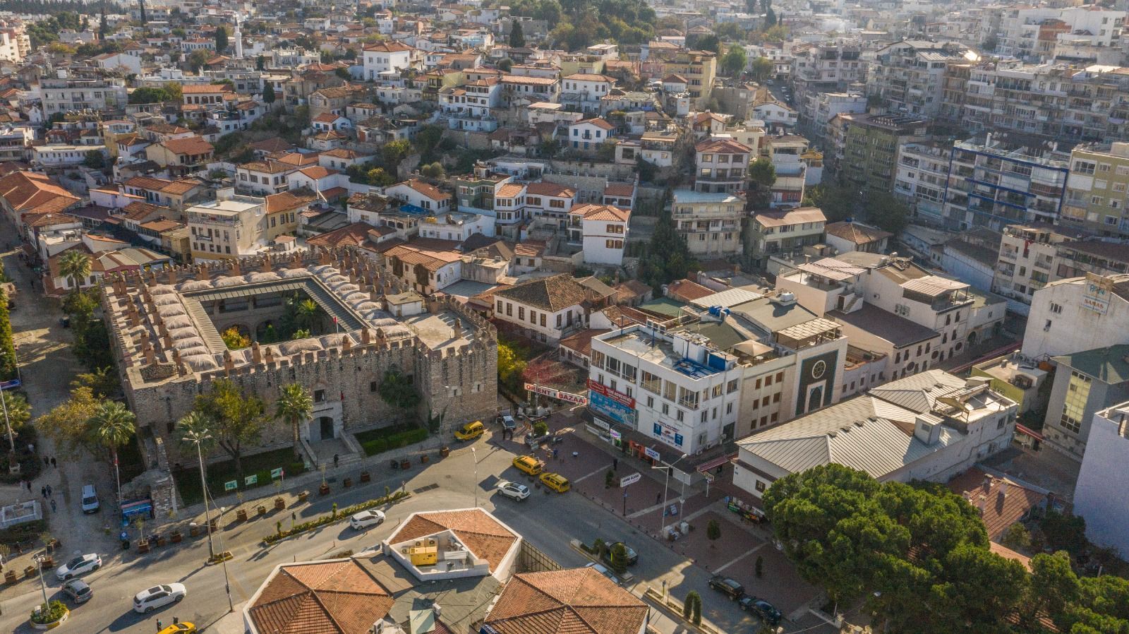 Une vue aérienne d’une zone urbaine densément peuplée, où se côtoient des bâtiments historiques et modernes, notamment une imposante structure ressemblant à un château et plusieurs immeubles commerciaux.