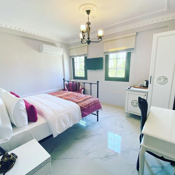 A bedroom with a bed, a desk, a chair, a nightstand, and a window.