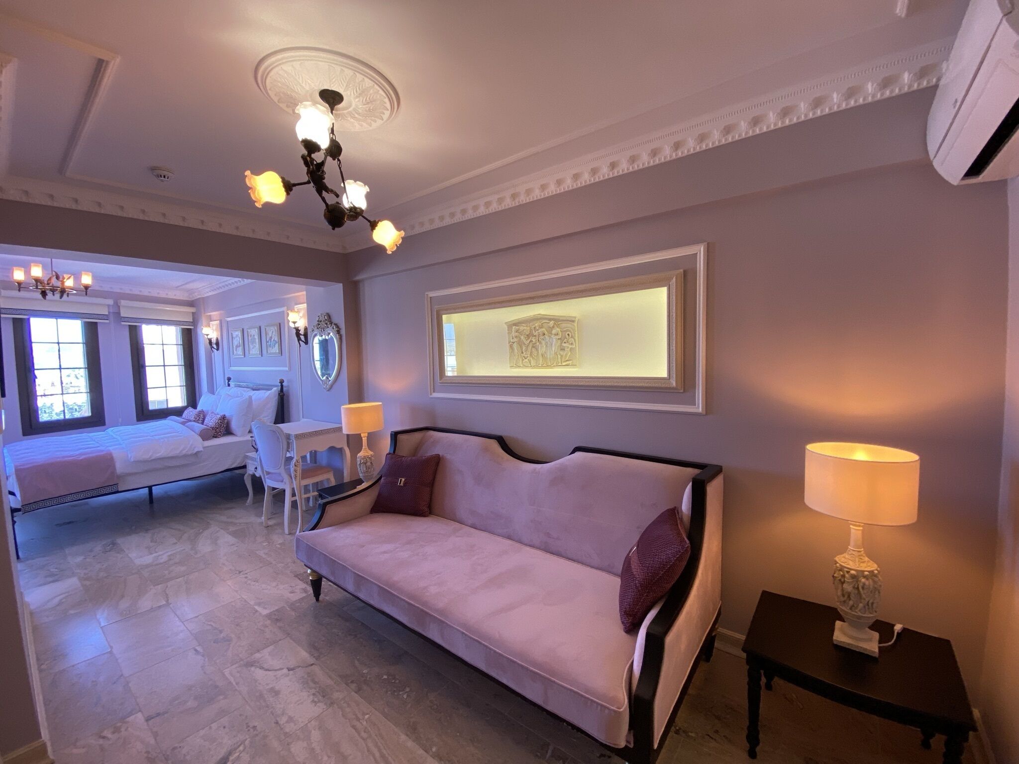 A spacious room with a large bed, a sofa, a desk, and a chandelier.