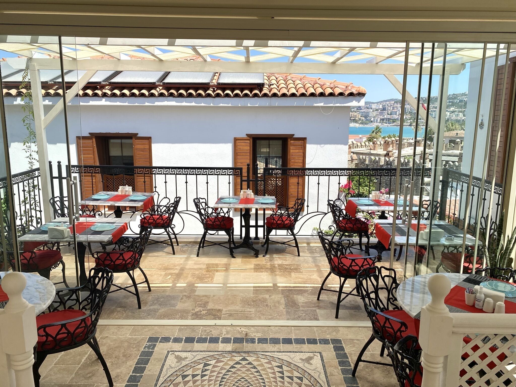 Eine Terrasse im Freien mit Tischen und Stühlen, einem Fliesenboden und Blick auf eine Stadtlandschaft.