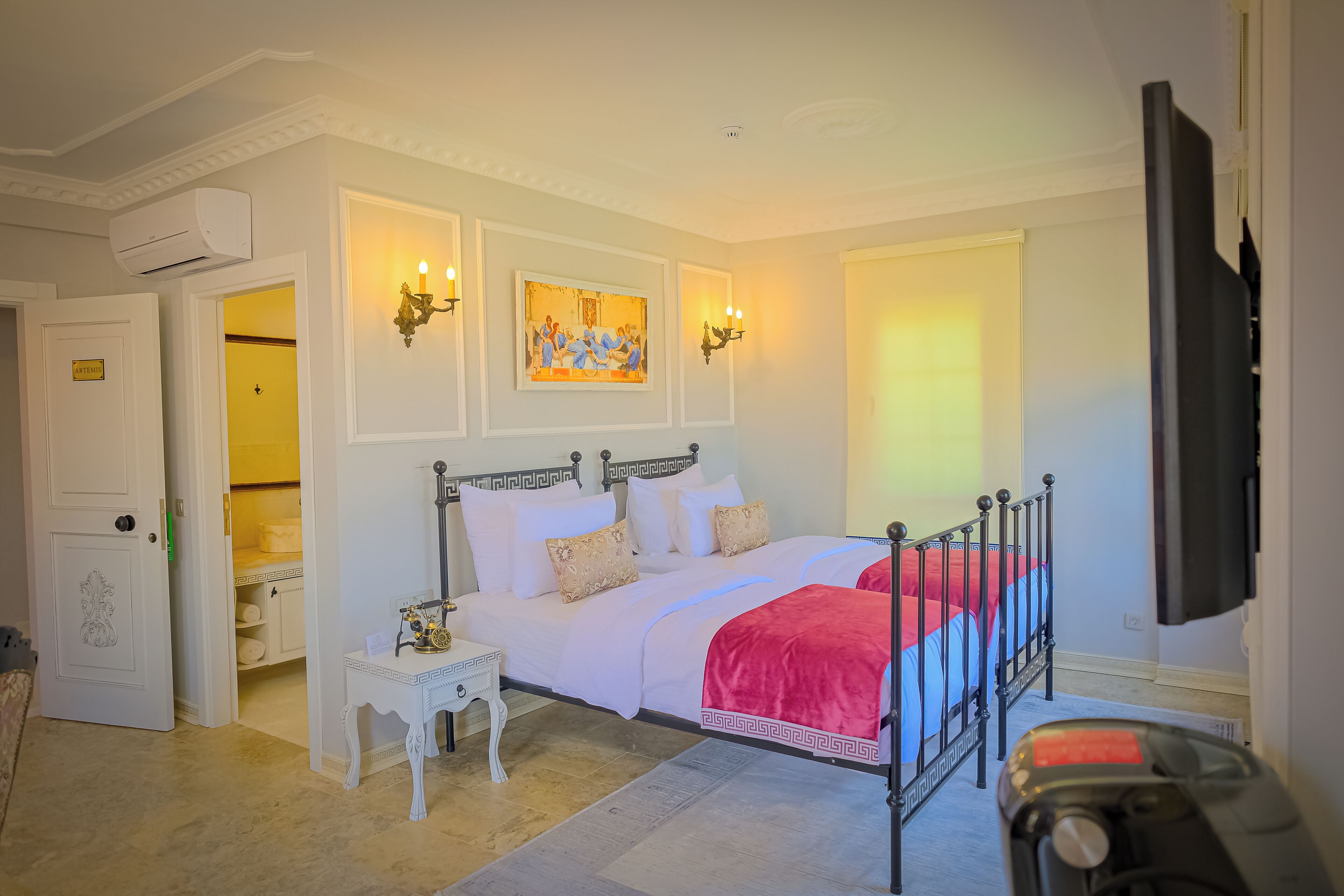 A bedroom with a bed, bedside table, artwork, and a television.