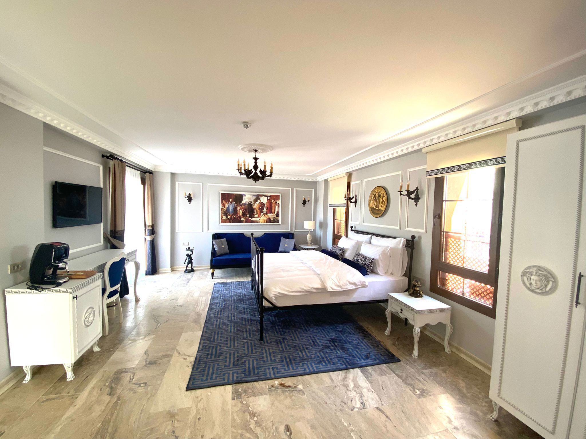 A spacious hotel room with a large bed, a desk with a coffee maker, a TV, and a blue sofa.