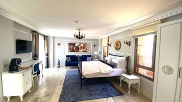 A spacious hotel room with a large bed, a desk with a coffee maker, a TV, and a blue sofa.