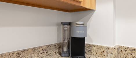 Una cocina con encimera de granito, cafetera Keurig y armarios de madera.