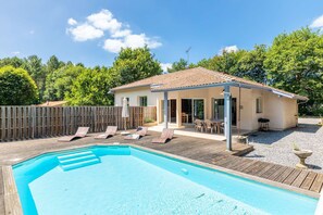 Uma casa com piscina, um pátio com espreguiçadeiras e um deck de madeira.