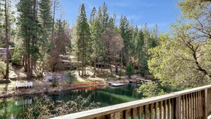 A wooden deck overlooking a calm river with a forested area and a building in the background.