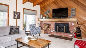 A cozy living room with a fireplace, a sofa, a patterned armchair, and a television.