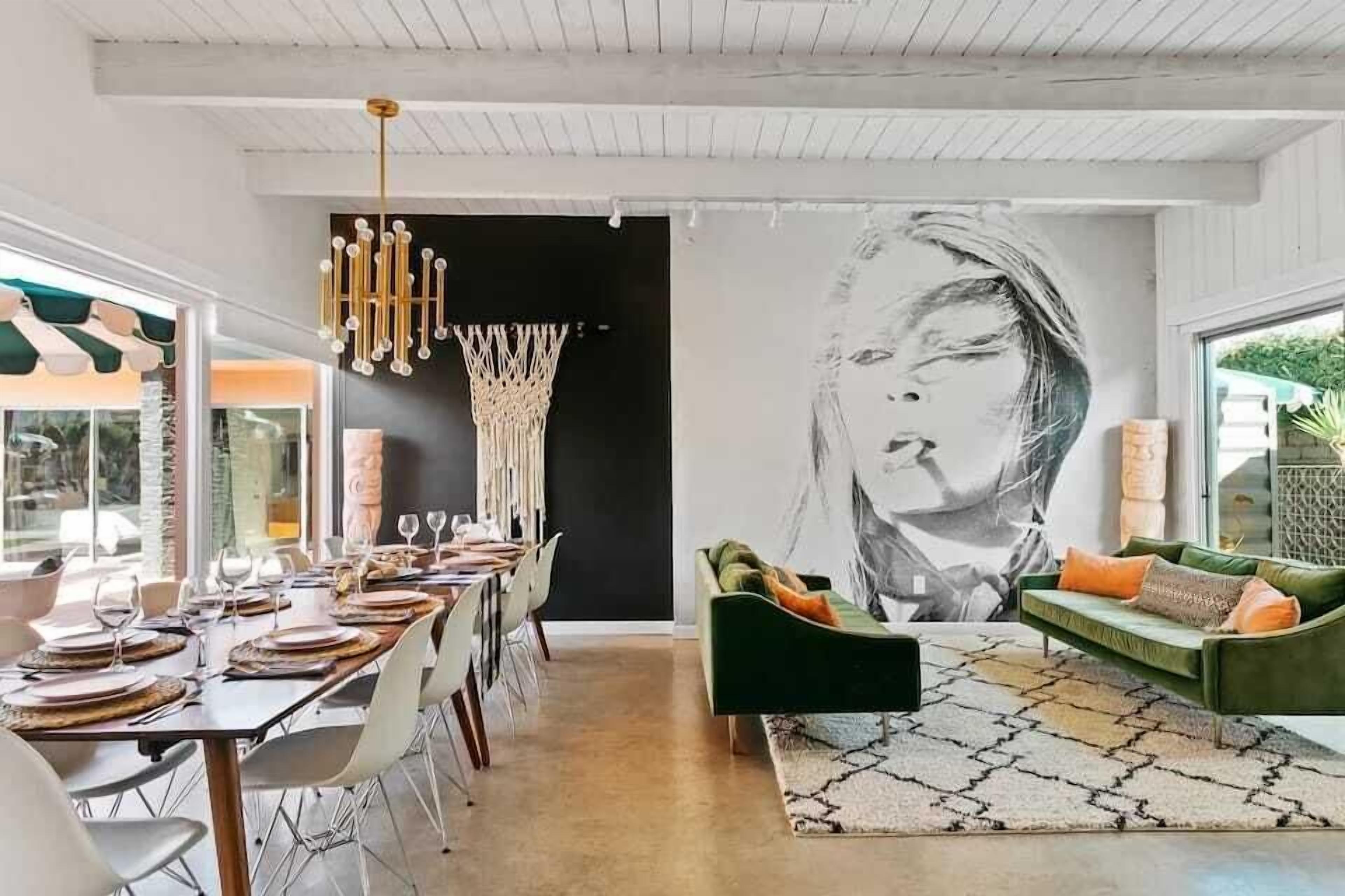 A dining area with a long table set for a meal, a green sofa in the living area, and a large abstract painting on the wall.