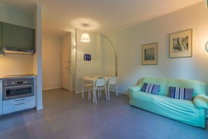 Un salon moderne comprenant un canapé, une table à manger avec des chaises, un coin cuisine avec une cuisinière et un couloir menant à une autre pièce.