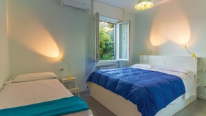 A bedroom with two beds, a window with a view of greenery, a ceiling light, and a wall-mounted air conditioner.