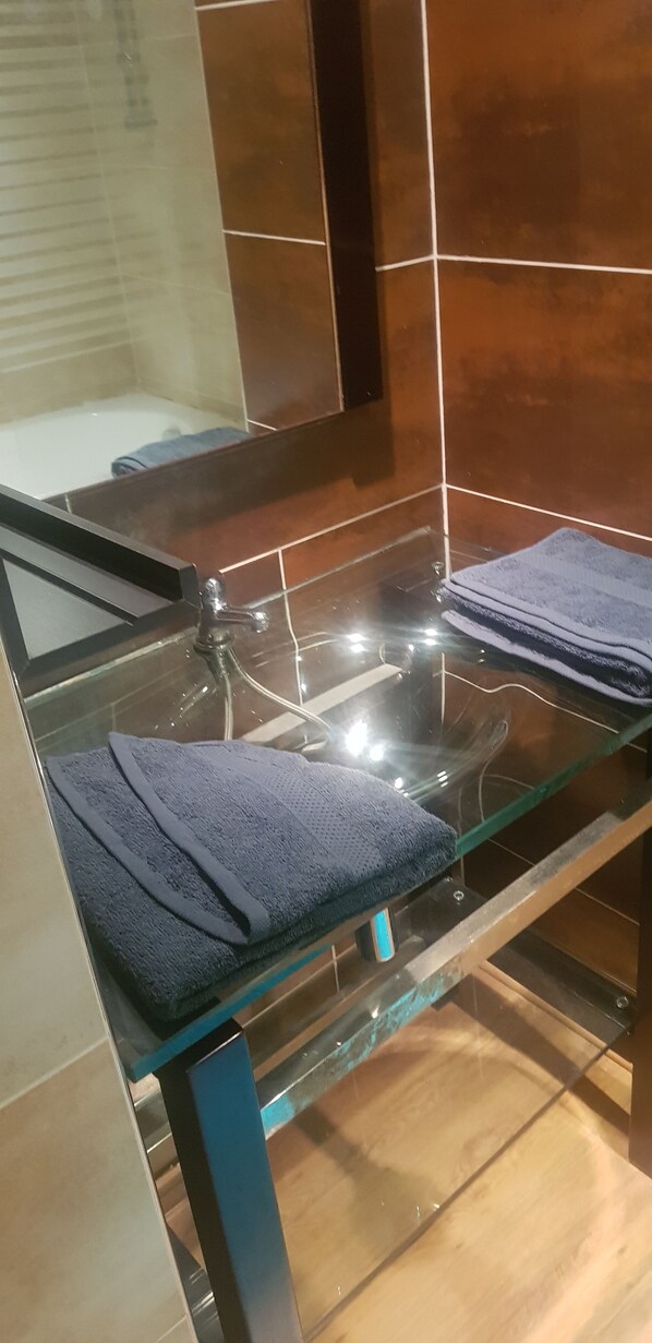 Een badkamer met een douchecabine van glas, een glazen wastafel en een handdoekrek met opgevouwen handdoeken.