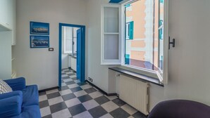 A room with a checkered floor, a blue sofa, a window with a view of buildings, and a door leading to another room.