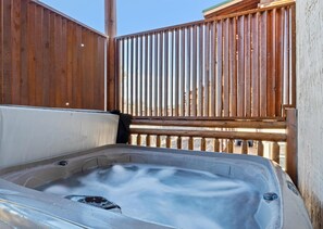 A hot tub with a wooden deck and a wooden fence in the background.