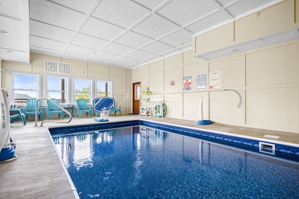 An indoor swimming pool with clear water, blue chairs, and safety signs on the walls.