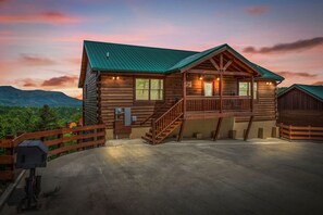 A log cabin with a porch, a staircase, and a view of the mountains.