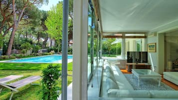 Sala de estar moderna com parede de vidro, piscina e vista para o jardim.