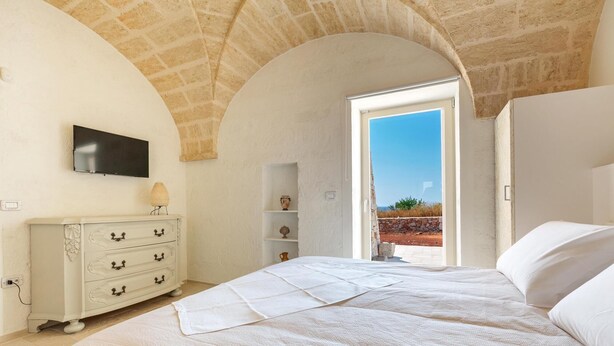 Quarto com cama, cômoda, televisão e vista para o exterior.