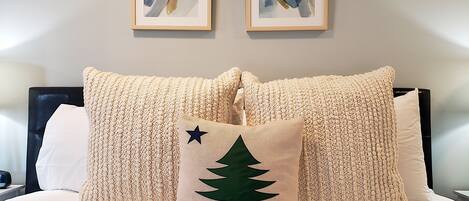 A neatly made bed with two large, textured pillows and a smaller pillow with a tree design. There are two framed artworks above the bed.