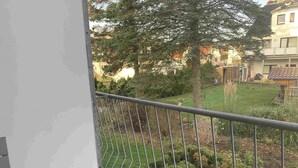 A balcony with a metal railing overlooking a garden with various plants and a building in the background.