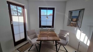 A dining room with a wooden table and two chairs, a window with a view, and a floor lamp.