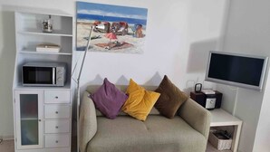 A living room with a sofa, a flat-screen TV, a microwave, a cabinet, and a painting of a beach scene.
