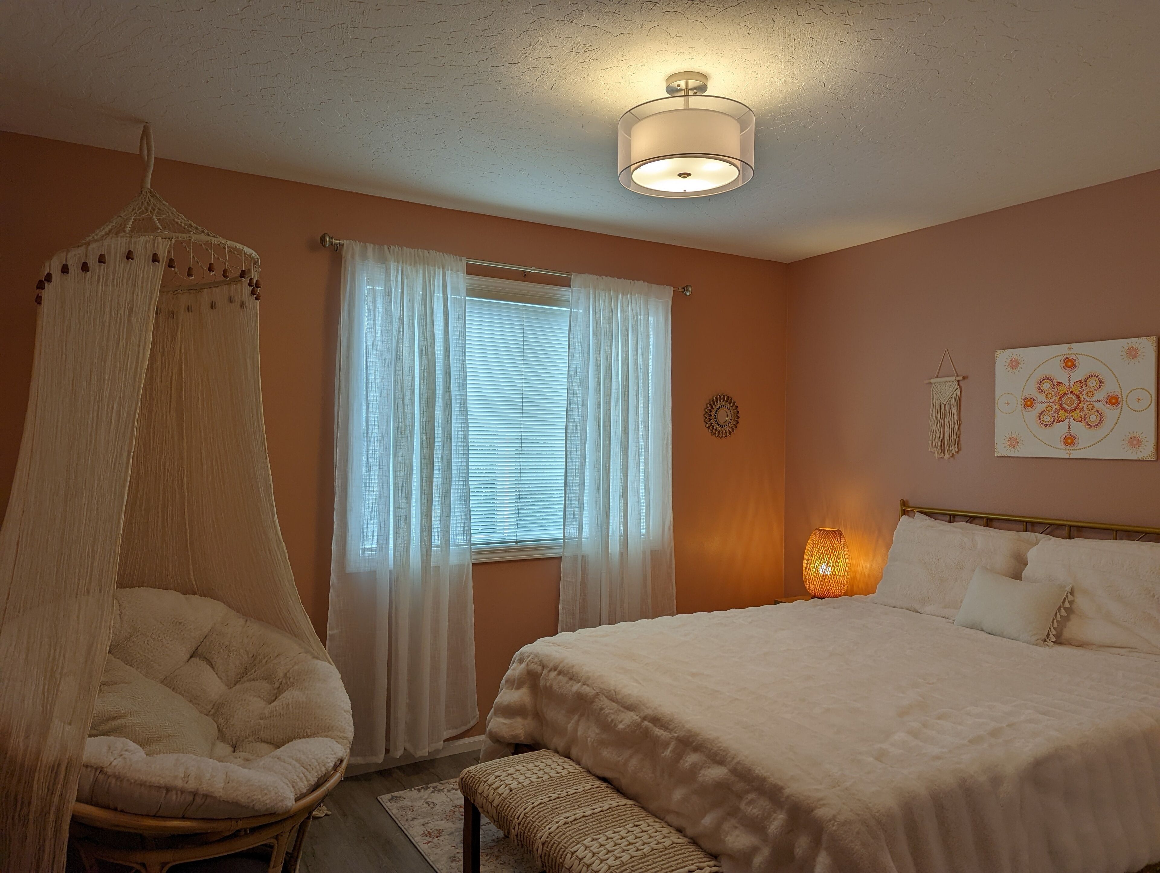 Une chambre à coucher avec un lit, un fauteuil suspendu, une fenêtre avec des rideaux, une horloge murale et un élément décoratif mural.