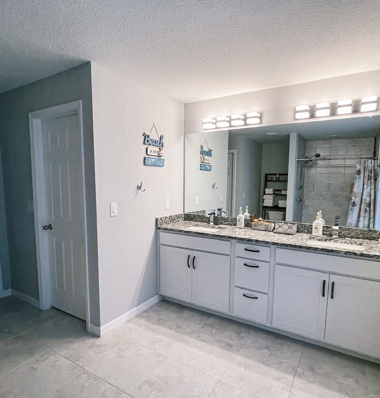 A bathroom with a large vanity, a mirror with lights, and a shower area.