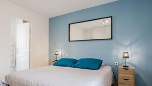 Een slaapkamer met een bed, twee nachtkastjes, een spiegel en een wandlamp.