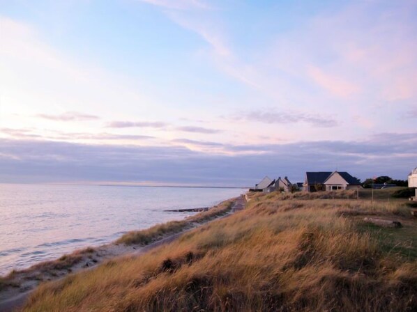 A coastal landscape with houses along the shore, a clear sky, and a calm sea.