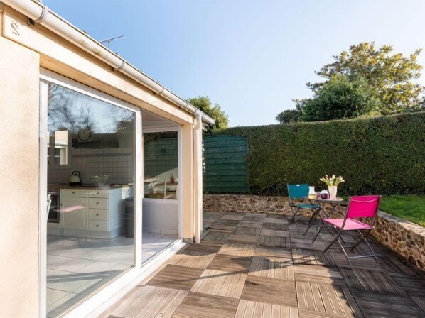 A patio with a wooden deck, a glass door leading to a kitchen, and two chairs.