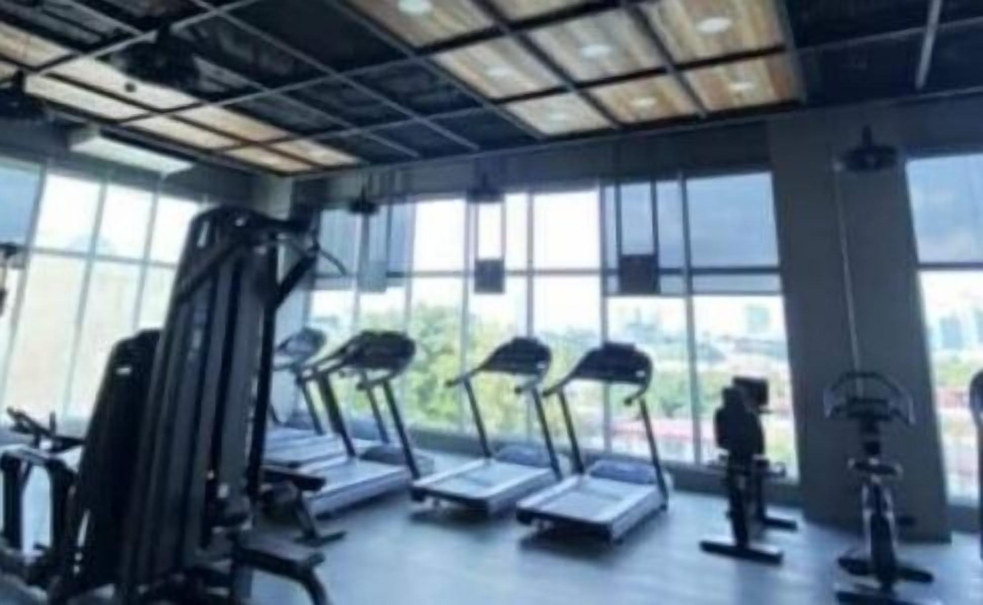 A gym with treadmills and exercise equipment, large windows, and a view of the city.