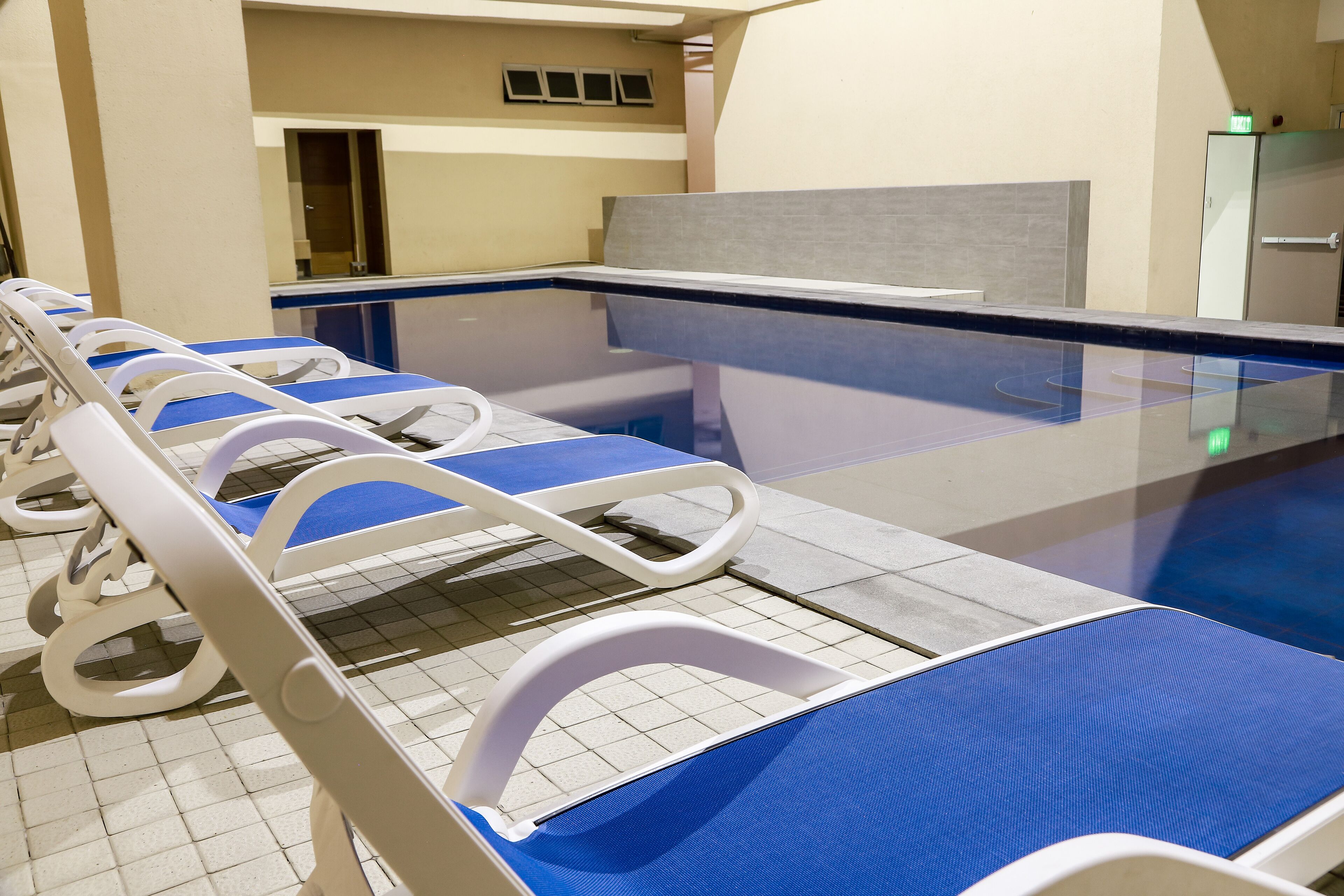 A row of hospital beds with blue covers, a tiled floor, and a glass partition.