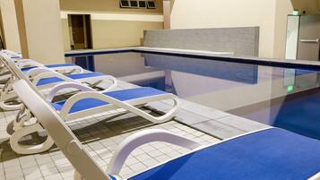 A row of hospital beds with blue covers, a tiled floor, and a glass partition.