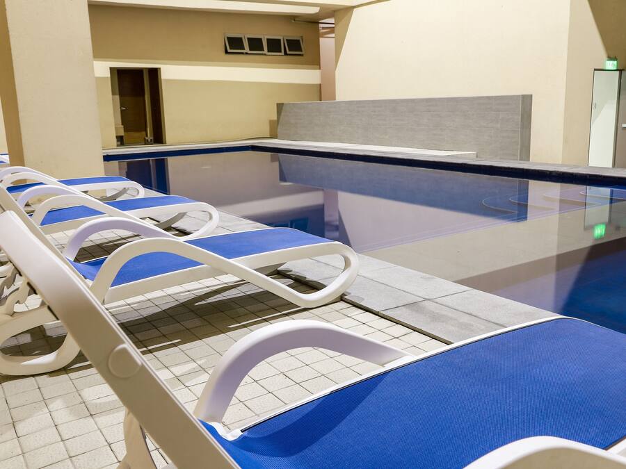 A row of hospital beds with blue covers, a tiled floor, and a glass partition.
