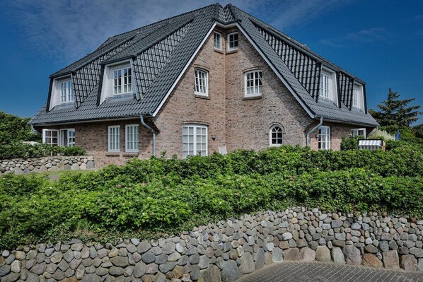 Et stort, toetagers hus med et stejlt tag, murstensvægge og mange vinduer.