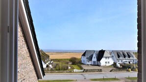 A coastal view with a white house, a paved driveway, and a stone wall. - Country house on the dune DU/07 - Country house on the dune (Sylt)