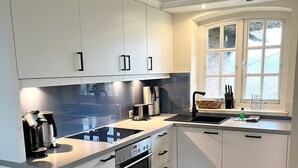 A modern kitchen with white cabinetry, a built-in oven, and a window with a view. - Landhaus am Watt - Landhaus am Watt DO/03 (Sylt)