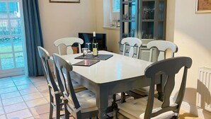 A dining area with a table and chairs, a cabinet with glassware, and a window with curtains. - Landhaus am Watt - Landhaus am Watt DO/03 (Sylt)