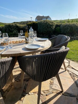 Un espace de restauration en plein air avec une table ronde, des chaises en osier et une bouteille de vin Bismark.