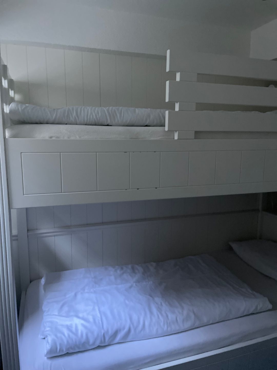 A bunk bed with white bedding and a lower single bed.