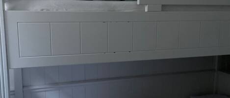 A bunk bed with white bedding and a lower single bed.