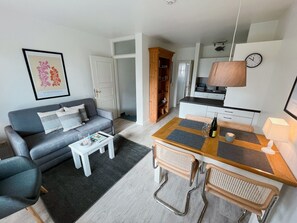 A modern living room with a grey sofa, a coffee table, and a dining area with a wooden table and chairs. - Raantem Hüs App. 04, - Raantem Hüs (Sylt)